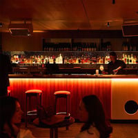 Two stools sit in front of red glowing bar at Honeydripper with bottles of spirits staked behind it