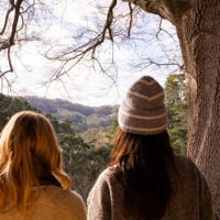 There's a view of rolling hills and tree branches between two people rugged up for the winter chill