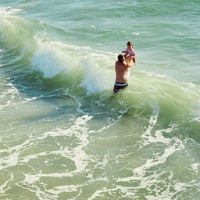A dad lifts up his child over the wave at Henley Beach 