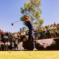 Professional golfer in a green shirt and cream pants holds up the golf ball to the spectators