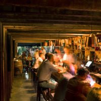 A dimly lit bar is filled with patrons on stools as the bartenders serve them