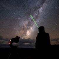 Stars litter the sky as a tour guide points a green laser into the sky mapping a constellation 