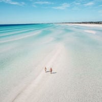 a light blue, shallow ocean with two people walking in the middle 