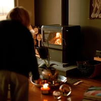 Someone lights a candle on the coffee table as the indoor fireplace burns to warm the house 