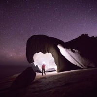 Someone stands under the Remarkable Rocks lighting it up with a torch as stars glow overhead 