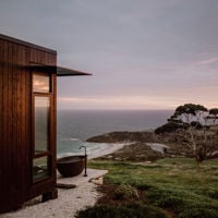 A wide-shot of a timber pod with a black bath out in the elements looking over Snelling Beach 