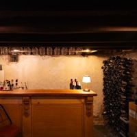A old bar with empty wine bottles lining the wall is lit by a lamp underground at Tread Lightly 