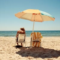 A man sits on a deck chair in the sand under a yellow umbrella at Normanville Beach 