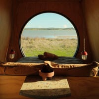 A circular window of a small wooden cabin looks out towards the lagoon 
