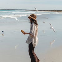 A girl in a sun hat with a scroll in hand surrounded by seagulls 