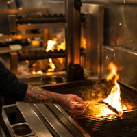 The open kitchen sees one chef plating while the other cooks over the open flame at Shobosho. 