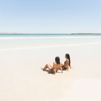 Two girls sit next to each other on the sand