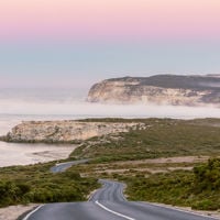 a long road leads towards a series of cliffs, with a pink and blue sky in the background
