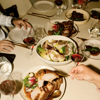 A table of hands reaching in for food and red wine at an event at Tasting Australia 